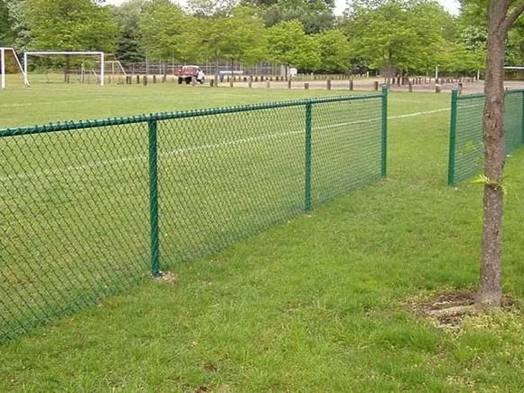 Green vinyl coated chain link fence along an athletic field with soccer goals in the background