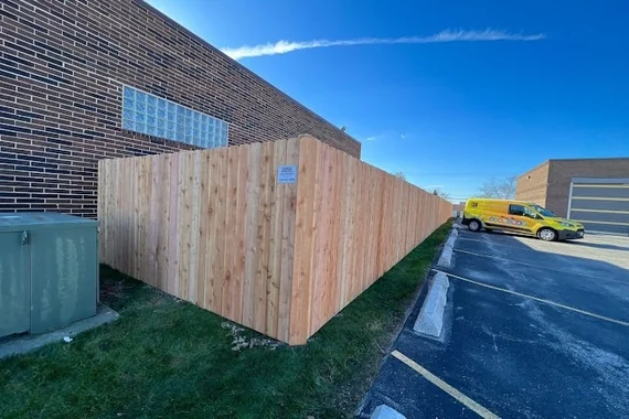 Wood privacy fence along the side of a brick commercial building next to a parking lot