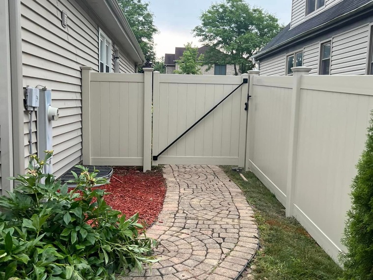 Tan vinyl privacy fence with a gate beside a paver walkway