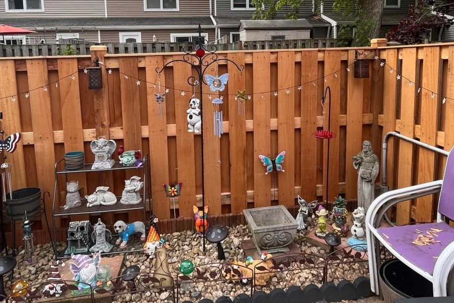Wood shadowbox fence enclosing a small gravel patio with garden ornaments, with townhomes behind